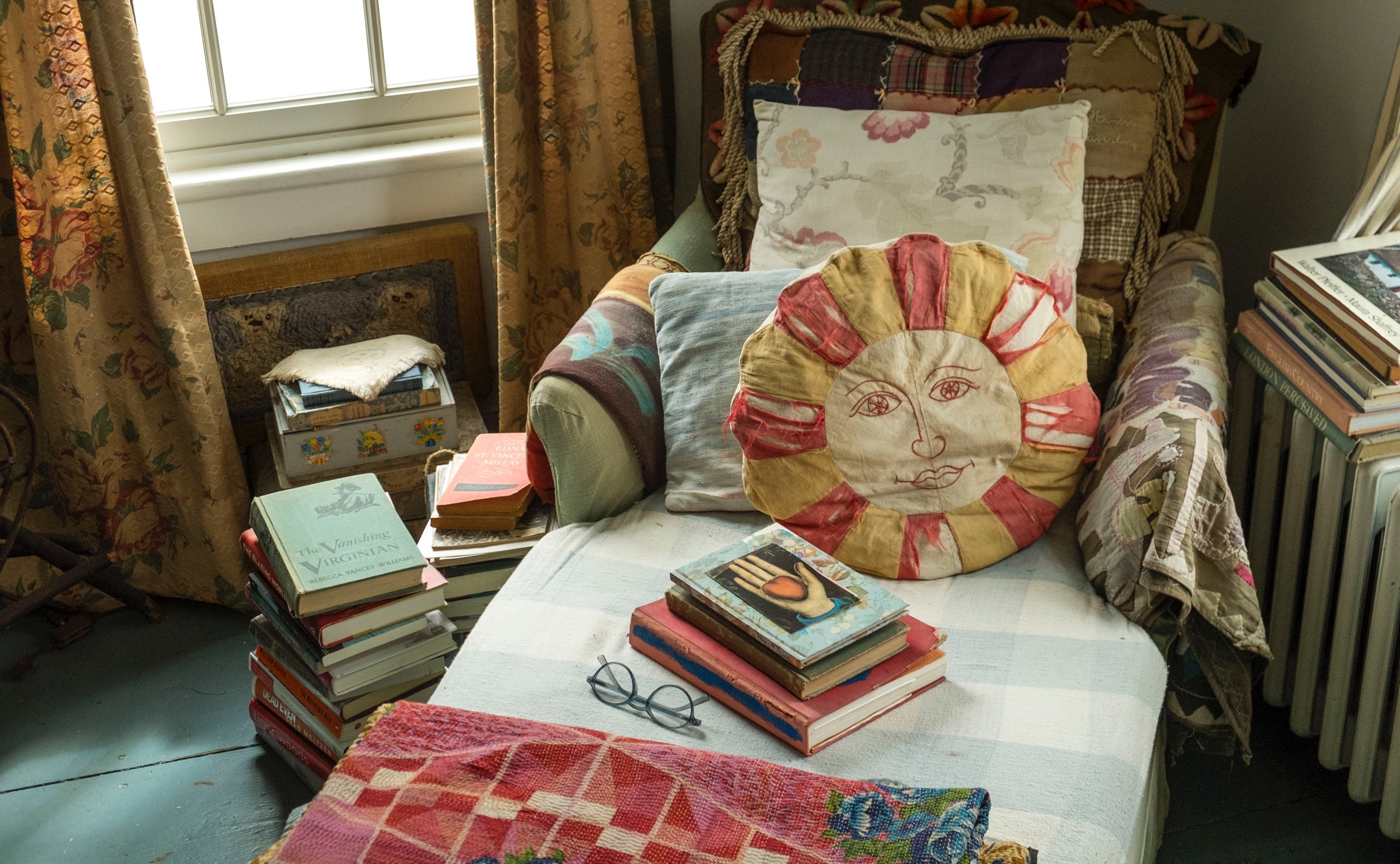 A cozy bedroom chaise surrounded by books and blanketed top-to-bottom with sun-faded coverlets, quilts, and textiles, softened with a collection of eclectic vintage pillows