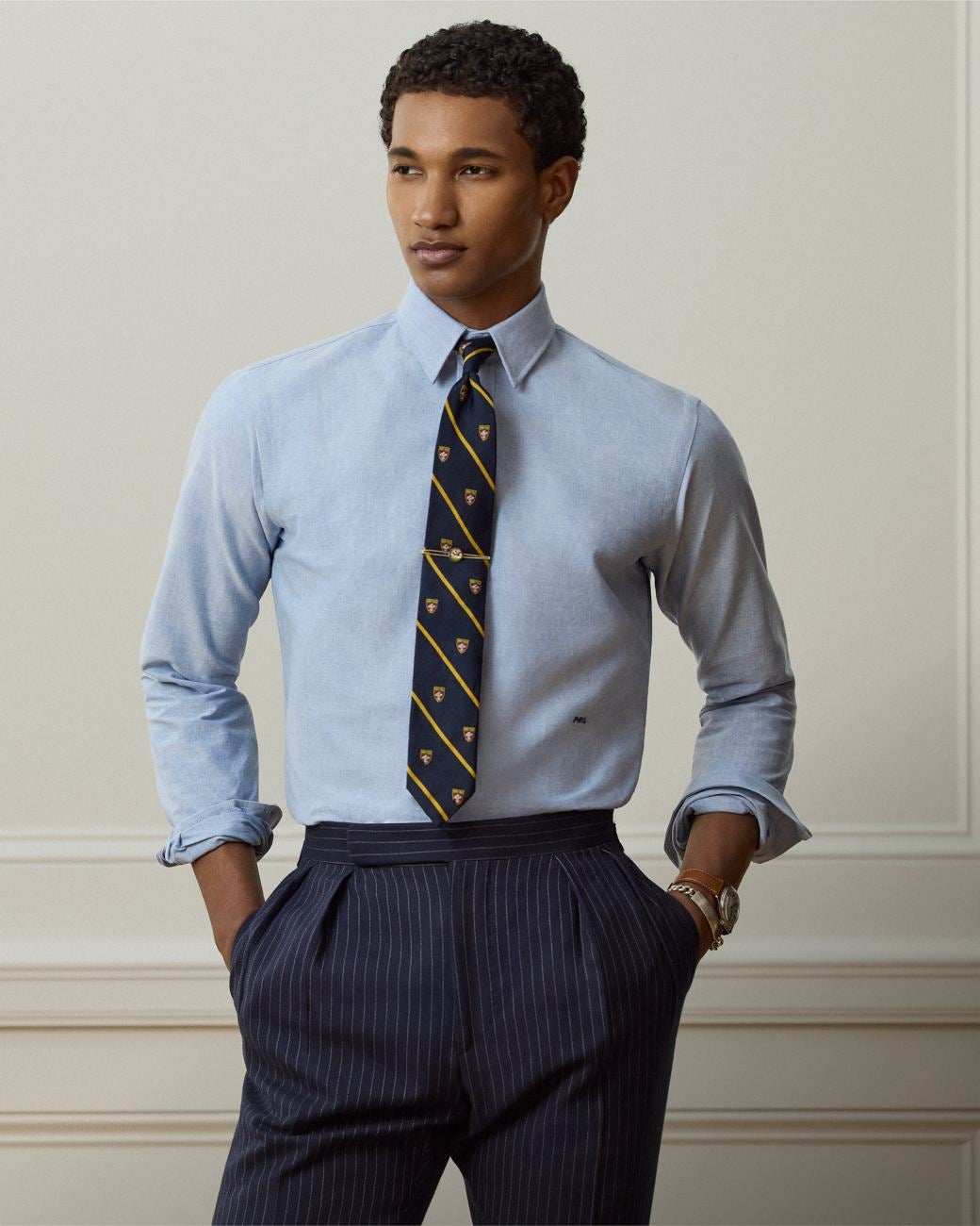 Man wears blue button-down shirt, tie, and navy pinstripe trousers.