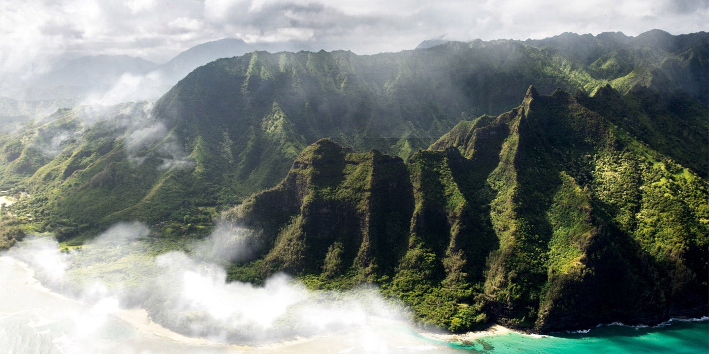 Photograph of cloudy green mountains above turquoise sea.